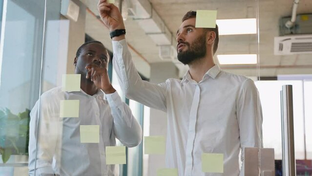 Brainstorming concept. Two men meeting at office and use post it notes to share idea. Sticky note on glass wall