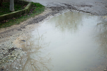 A large muddy puddle on the road on a rainy day. Close-up. Hopelessness and dirt. Space for text.