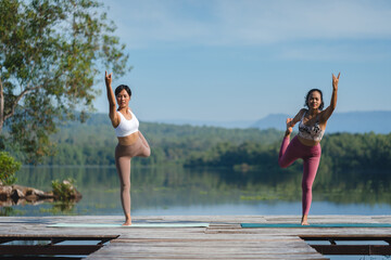 Fototapeta na wymiar Athlete women, two female friends is doing yoga pose by the lake in the early morning, couple practicing exercise and training workout outdoor. Wellness and well being recreation, meditation balance.