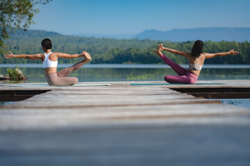 Athlete women, two female friends is doing yoga pose by the lake in the early morning, couple...