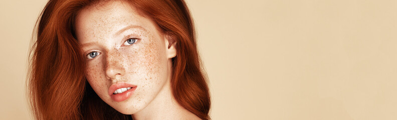 A close-up portrait of a young woman with striking red hair and a complexion dotted with freckles,...