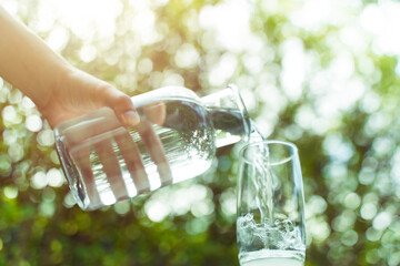 Water from bottle pouring into glass on table in the morning, bokeh background. clean water for a...