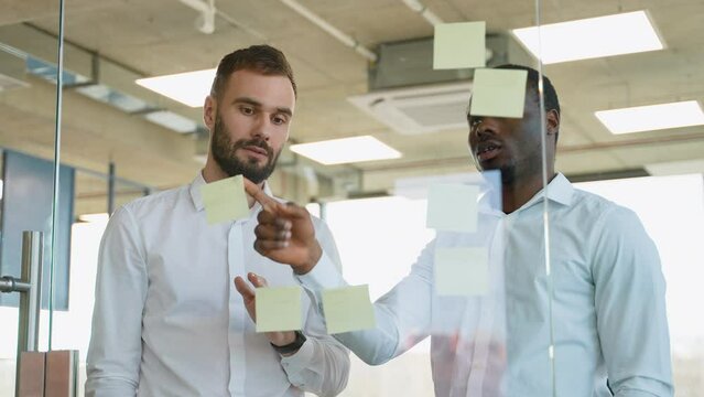 Brainstorming concept. Two men meeting at office and use post it notes to share idea. Sticky note on glass wall