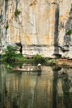 Vietnamese woman fishing for crabs on a boat along the limestone cliff in Ninh Binh, Vietnam