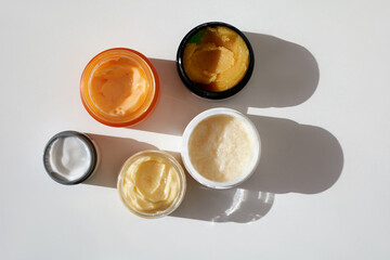 Different containers with natural herbal moisturising skin care products scrub, cream, peeling, green tea tree lotion and chea butter, top view, white background