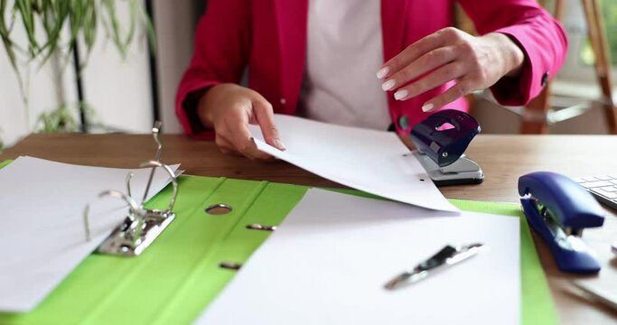 Hands of secretary manager punch holes in paperwork in office. Organization of document flow in company