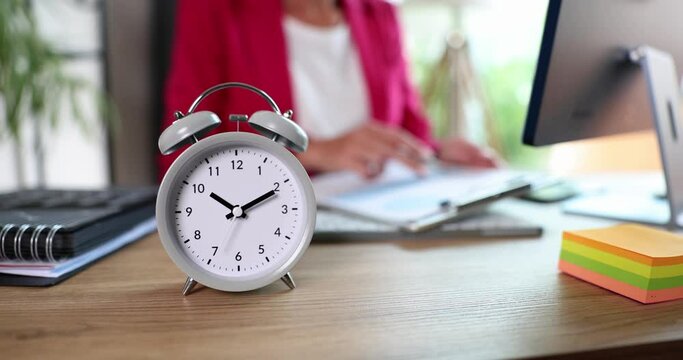 Alarm clock at ten o'clock in businesswoman marketer analyst works with documents in office. Remote work time control