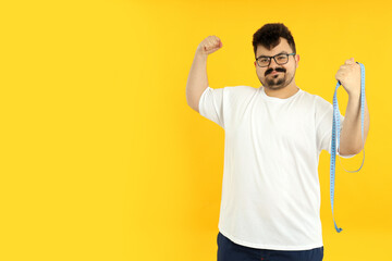 A fat man shows his muscles, on a yellow background. - obrazy, fototapety, plakaty