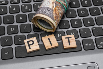 Napis PIT na klawiaturze laptopa obok polskich pieniędzy 