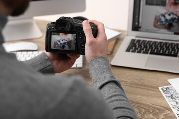 Professional photographer with digital camera at wooden table indoors, closeup