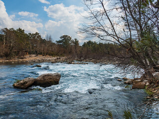 Milky blue river water flows quickly along its bed.Rocks in the water create rapids, waves and foam. Beautiful landscape of a mountain river in Turkey.The concept of traveling rafting on a kayak, boat
