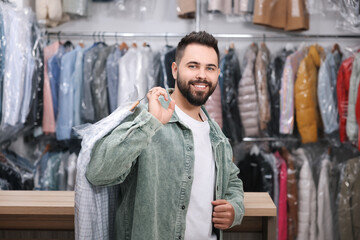 Dry-cleaning service. Happy man holding hanger with shirt in plastic bag indoors