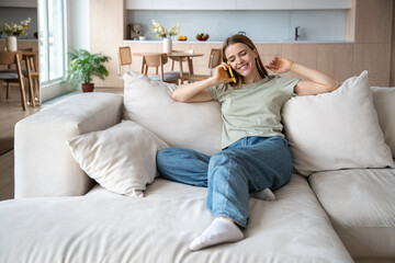 Glad positive joyful middle-aged caucasian woman lying relaxed on comfortable sofa in modern apartment, speaking over mobile phone, having pleasant conversation, funny discussion with friend, workmate