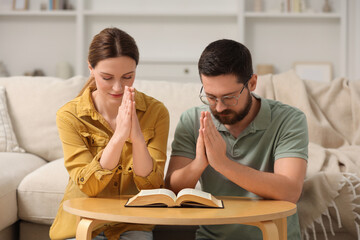 Family couple praying over Bible together at table indoors