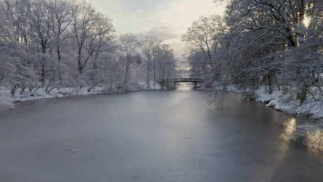 Flying through trees in winter snow landscape towards over frozen river