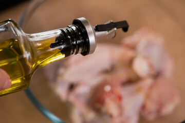 A hand pours olive oil into raw chicken. Preparing Ingredients