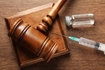 Law concept. Gavel, syringe and glass vial on wooden table, top view