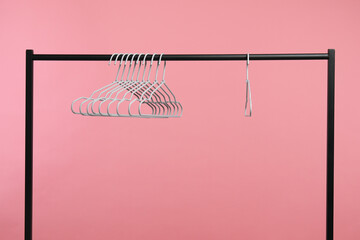 Empty clothes hangers on rack against pink background