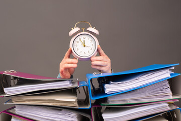 Alarm clock standing next to pile of file folders, burnout, stress and overworked, pressure at...