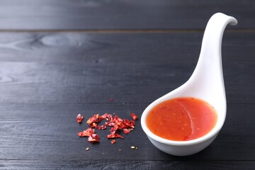 Chili sauce in spoon on black wooden table, closeup. Space for text