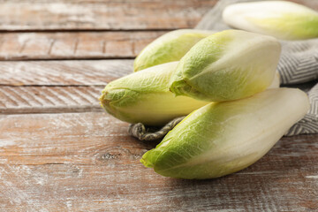 Fresh raw Belgian endives (chicory) on wooden table, closeup. Space for text