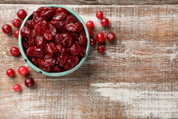 Tasty dried cranberries in bowl and fresh ones on rustic wooden table, top view. Space for text