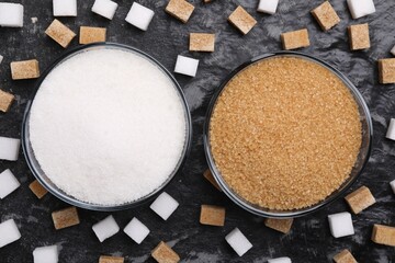 Different types of sugar in bowls on dark gray textured table, flat lay