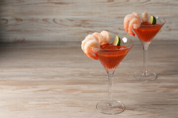 Tasty shrimp cocktail with sauce and lime in glasses on wooden table, space for text