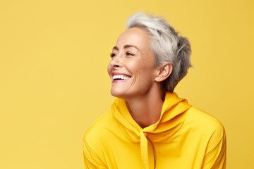 Mature woman in yellow hoodie smiling and looking up over yellow background.