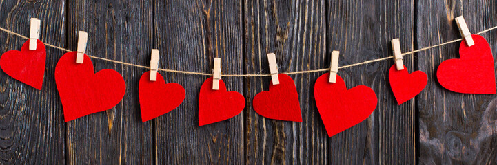 Red hearts on a rope with clothespins, on a black wooden background. Greeting card for Valentine's Day, banner.
