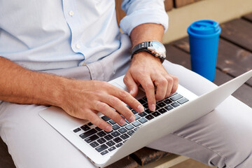 A successful businessman sits on a bench on the street and works at a laptop during a break