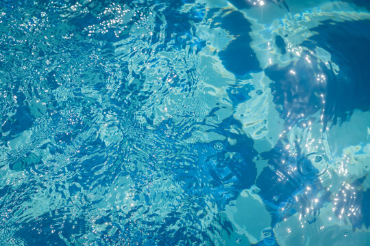 background with blue water surface of swimming pool with tiles and ripples in sun light