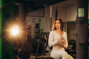 Young woman drinking water and taking a break after workout in gym,