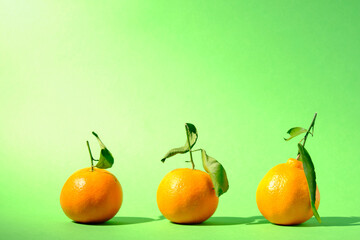Three sunlit clementines against a seamless green background