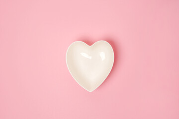 A white heart-shaped plate on pink background. The concept of love and happiness on Valentine's Day