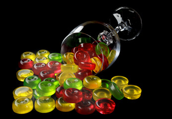 Many lollipops spill out from an overturned glass goblet. Multi-colored candies in a glass on a black background.