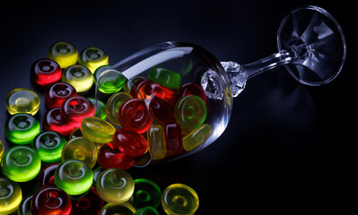 Many lollipops spill out from an overturned glass goblet. Multi-colored candies in a glass on a black background.