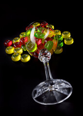A lot of candy canes are scattered from an overturned glass goblet. Multi-colored candies in a glass on a black background.