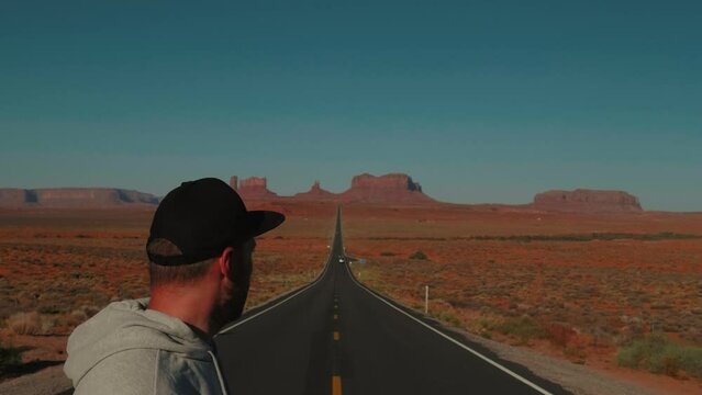Close-up shot of young adult man turning to look around on highway at epic cinematic sunny sandstone desert of Arizona.