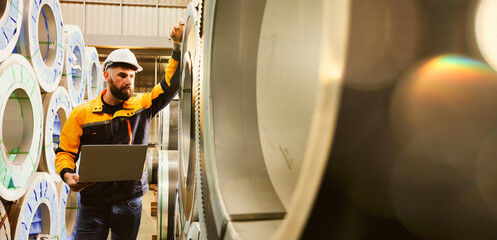 Male technician inspects stock in the raw material storage area steel coils large rolls metal...