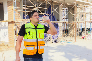 Male worker sweating and thirsty while working on a building construction site in the hot summer...