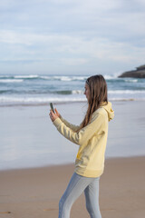 Woman on the seashore taking a photo with her cell phone