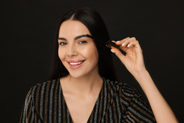 Beautiful young woman applying mascara on black background