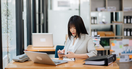 Successful Asian Businesswoman Analyzing Finance on Tablet and Laptop at modern Office Desk tax, report, accounting, statistics in office.