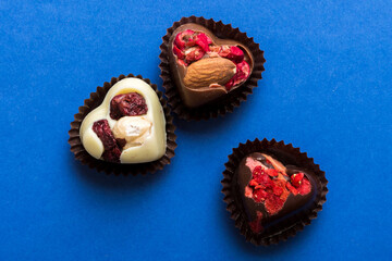 chocolate sweets in the form of a heart with fruits and nuts on a colored background. top view with space for text, holiday concept