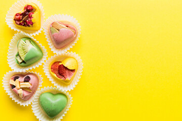 chocolate sweets in the form of a heart with fruits and nuts on a colored background. top view with space for text, holiday concept