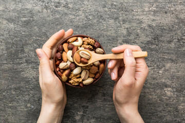 Woman hands holding a wooden bowl with mixed nuts Walnut, pistachios, almonds, hazelnuts and...