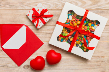 Red envelope with candy and gift box and Valentines hearts on colored background. Flat lay, top view. Romantic love letter for Holiday concept