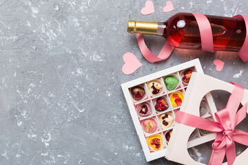 Bottle of red wine on colored background for Valentine Day with gift and chocolate. Heart shaped with gift box of chocolates top view with copy space
