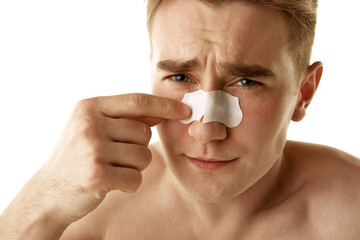 Young shirtless man taking care after face, applying pore cleansing, anti-blackhead patch strip on...